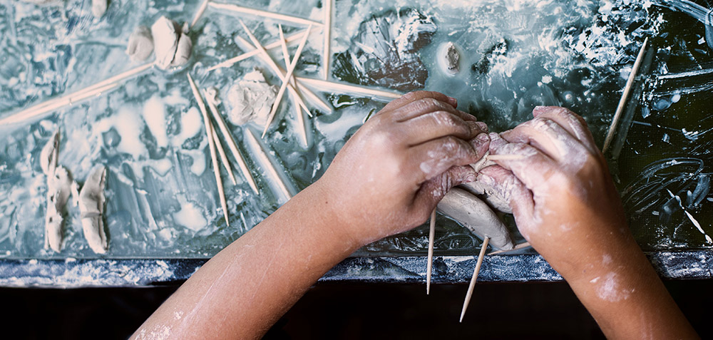 kids hands molding clay on a messy table by Samantha hurley